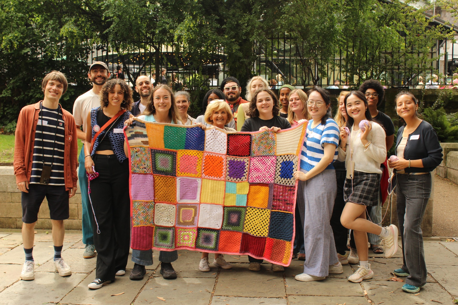 A group of people holding up a patchwork cloth they have knitted