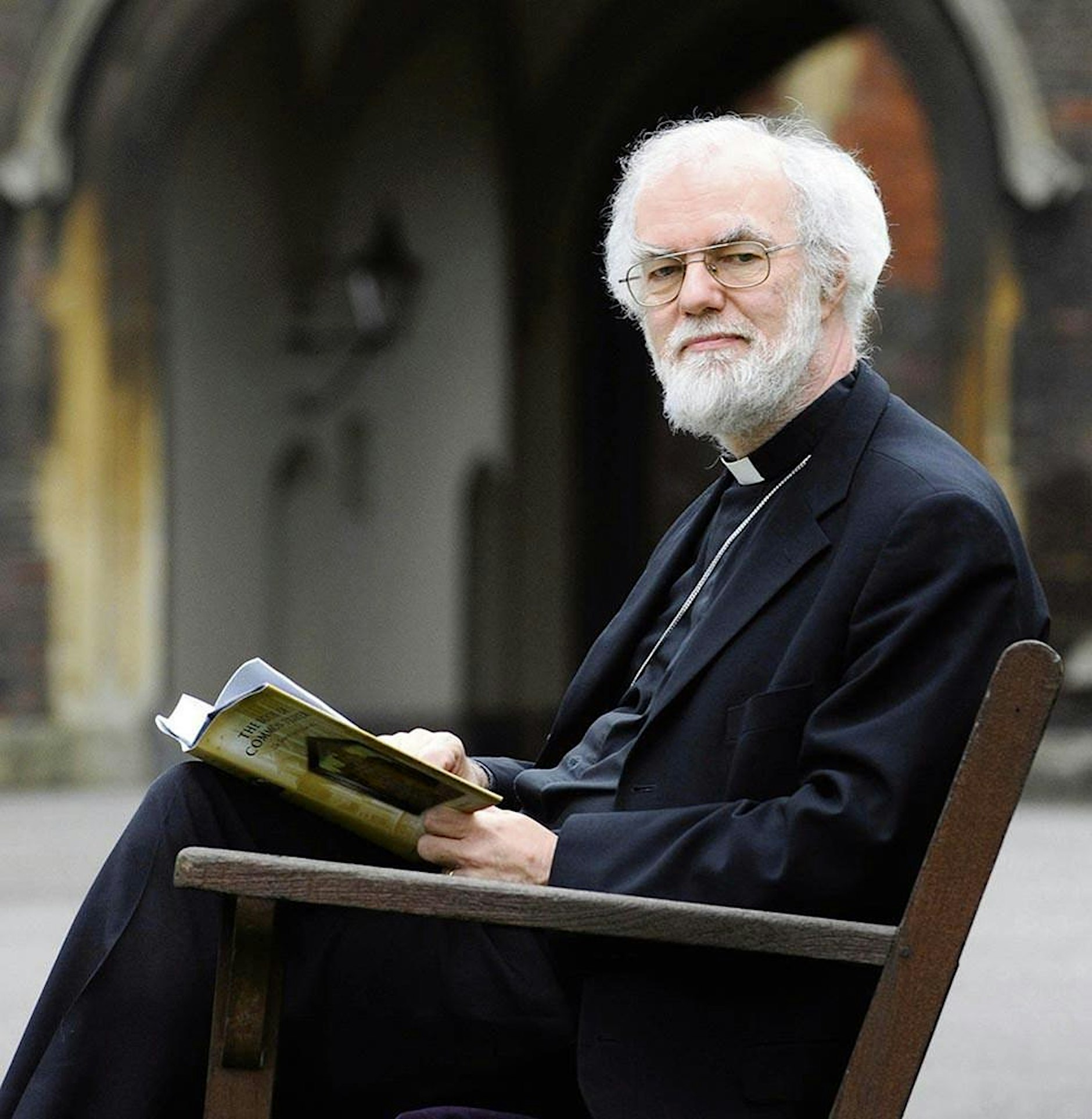 Rowan Williams sitting on a chair reading a book